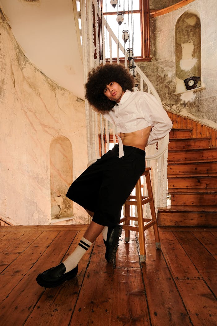 Fashionable individual posing indoors with afro hairstyle and modern attire.